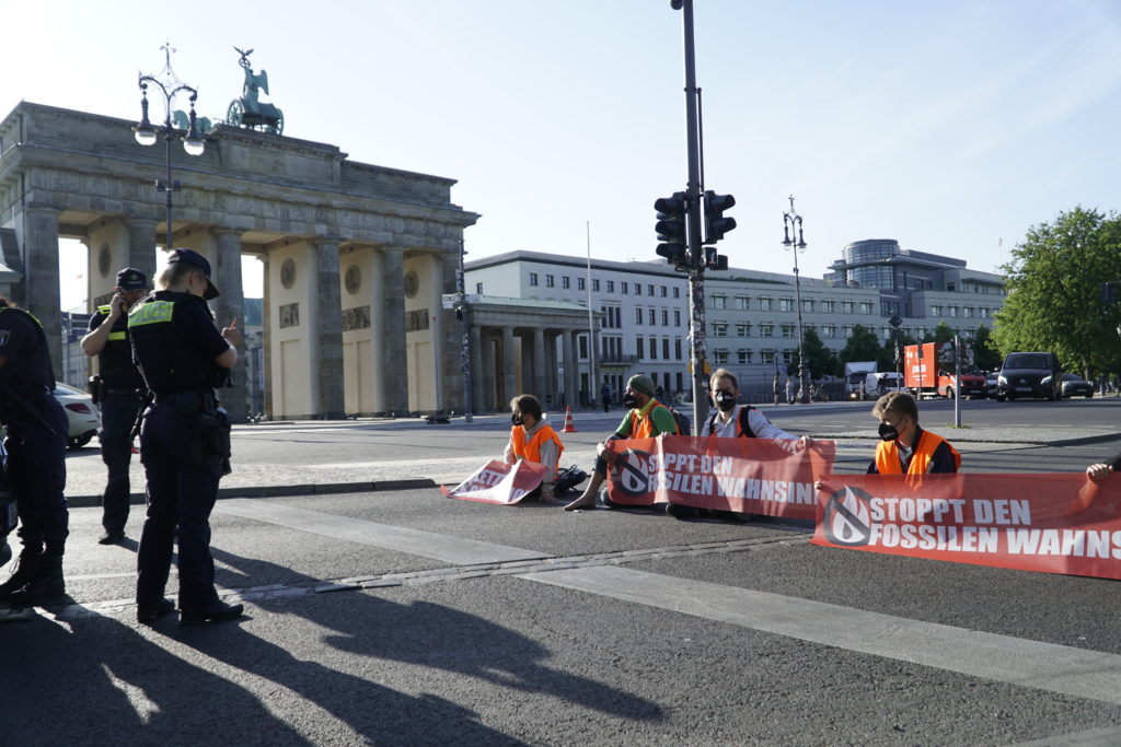 Sitzblockade auf der Straße vor dem Brandenburger Tor. Die Blockierenden halten Banner mit der Aufschrift "Stoppt den fossilen Wahnsinn" in den Händen.
