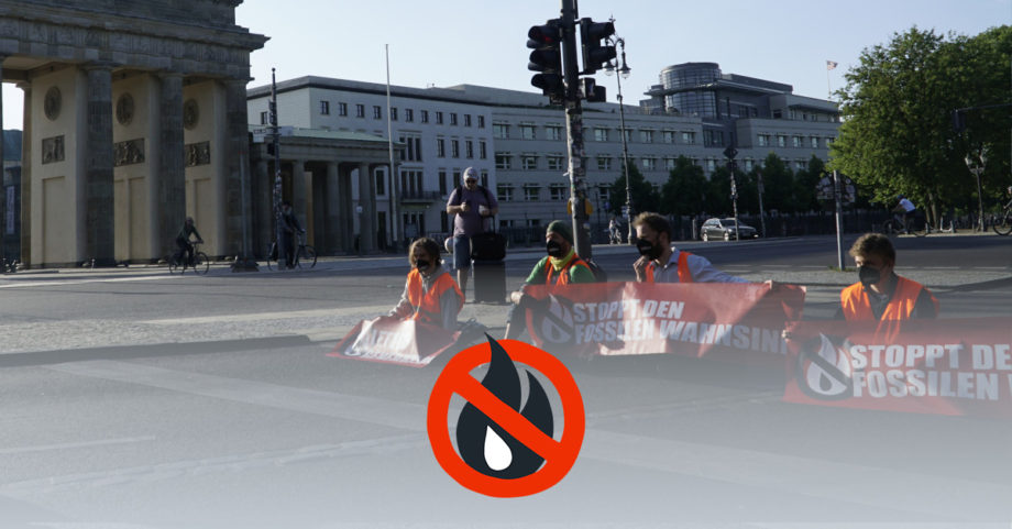 Sitzblockade auf der StraĂe vor dem Brandenburger Tor. Die Blockierenden halten Banner mit der Aufschrift "Stoppt den fossilen Wahnsinn" in den HĂ€nden.