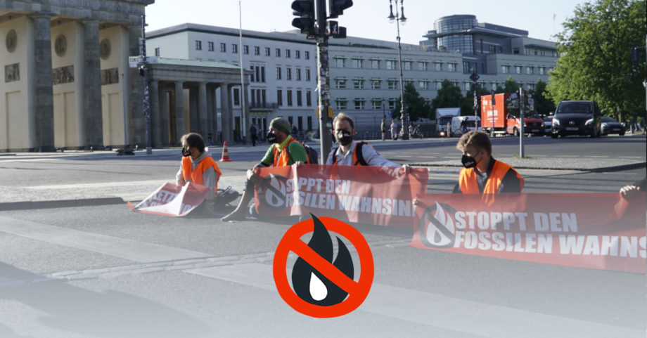 Sitzblockade auf der StraĂe vor dem Brandenburger Tor. Die Blockierenden halten Banner mit der Aufschrift "Stoppt den fossilen Wahnsinn" in den HĂ€nden.