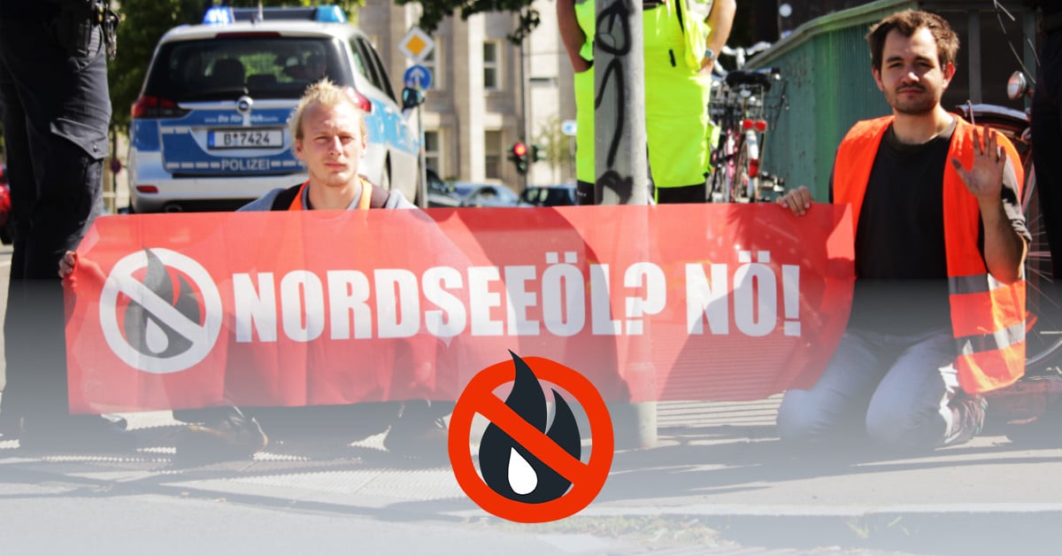 Two people in high-visibility vests block the street. They hold a banner that says "North Sea oil? Nope!" in the hands.